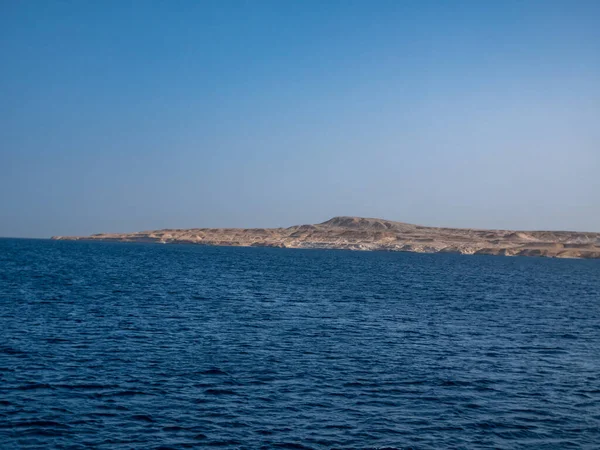 Large deserted uninhabited island on the blue sea horizon. — Stockfoto