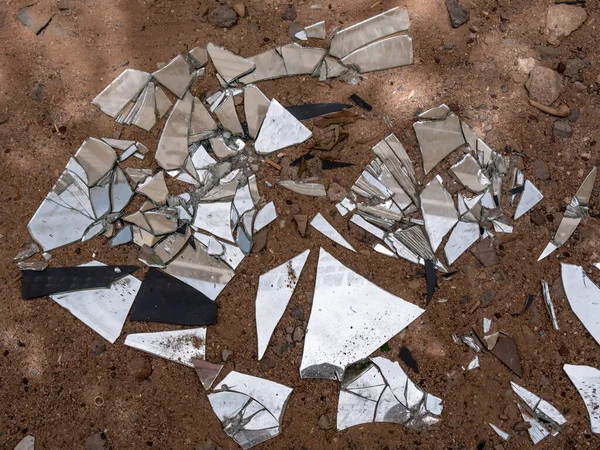 Shards of a broken mirror are scattered on the ground. Environmental pollution.