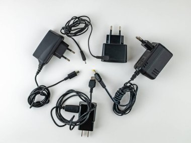 Akıllı telefonların ve cep telefonlarının boş bataryalarını şarj etmek için dört siyah şarj aleti. Çeşitli cihazları şarj etme kavramı. Beyaz arkaplan ve kopyalama alanı.