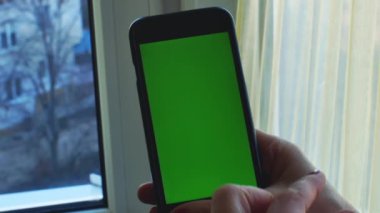 Close-up of female hands holding a smartphone and touching the screen. Chroma key. Green screen. Copy space.