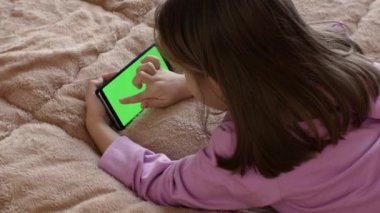 7-8 yaşlarında küçük bir kız, önceden ayarlanmış yeşil ekranlı akıllı telefon kullanıyor. Birkaç çeşit jest - sola-sağa kaydırma, dokunma. Ekran düzeni için ideal. Krom anahtar. yeşil ekran.