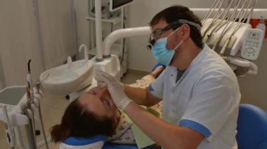 The patient is in the dental chair with her mouth open while the dentist treats her teeth. Health care