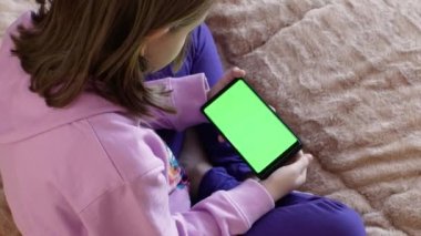 7-8 yaşlarında küçük bir kız, önceden ayarlanmış yeşil ekranlı akıllı telefon kullanıyor. Birkaç çeşit jest - sola-sağa kaydırma, dokunma. Ekran düzeni için ideal. Krom anahtar. yeşil ekran.