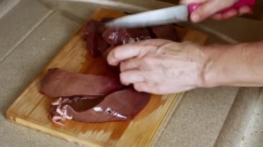 A housewife cuts pork liver meat with a knife on a wooden kitchen board in a home kitchen. Close-up of female hands. Cook at home. Home atmosphere in the home kitchen. High quality 4k footage