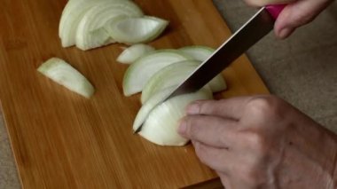 Close-up of female hands cutting fresh onions on a wooden cutting board in the kitchen. Slice. To cook.