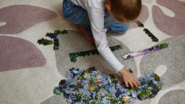 A girl sitting on a rug chooses colorful puzzle pieces and sorts them. Preschool development of children. High quality 4k footage