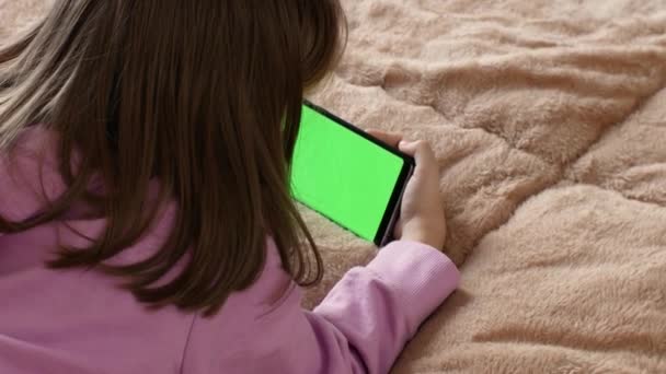 Close-up of a mobile phone in the hands of a little girl using her smartphone with green screen chroma key mockup.