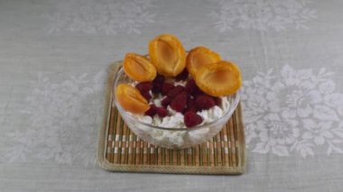 Glass bowl with cottage cheese, red raspberries, and slices of ripe yellow apricots. Natural products are healthy. Healthy and delicious food.