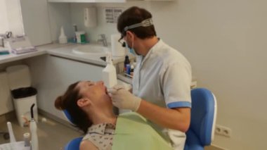 The patient is in the dental chair with her mouth open while the dentist treats her teeth. Health care