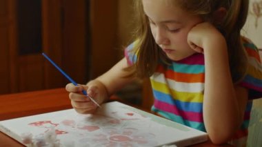 A pretty little artist paints in watercolor on white paper while sitting at a table. Artists studio. Learning to draw.