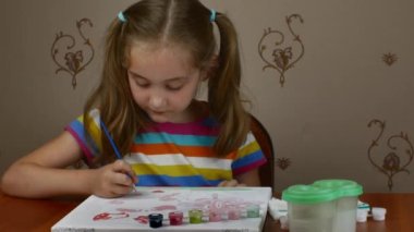 A girl of 7-8 years old sits at a table and draws a picture with paints on white paper. teaching children to draw.