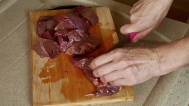 A housewife cuts pork liver meat with a knife on a wooden kitchen board in a home kitchen. Close-up of female hands. Cook at home. Home atmosphere in the home kitchen. High quality 4k footage