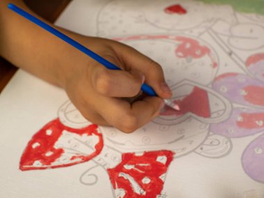 A little girls hand drawing with a brush and watercolor paints on white paper. Close-up. View from above. Creativity develops children.