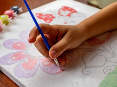 A little girls hand drawing with a brush and watercolor paints on white paper. Close-up. View from above. Creativity develops children.