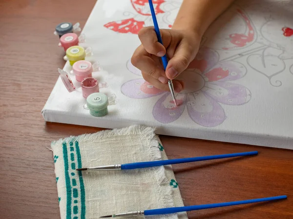 A little girls hand drawing with a brush and watercolor paints on white paper. Close-up. View from above. Creativity develops children.