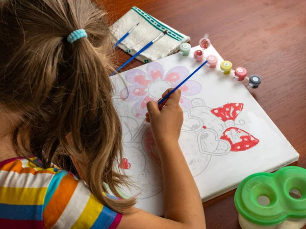 A little girls hand drawing with a brush and watercolor paints on white paper. Close-up. View from above. Creativity develops children.