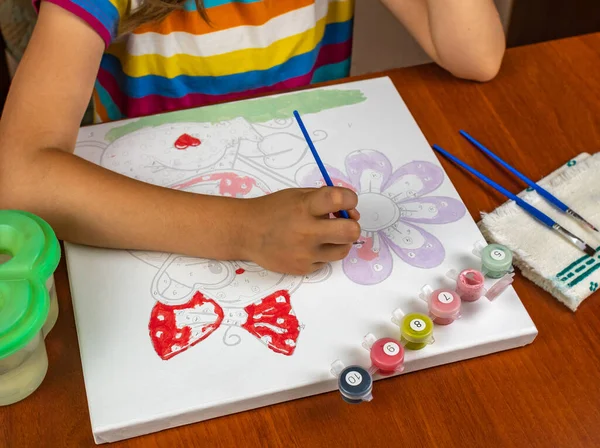 A little girls hand drawing with a brush and watercolor paints on white paper. Close-up. View from above. Creativity develops children.