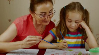 An adult woman with a little girl draws on paper with colored watercolors. Grandmother and granddaughter study painting. Preschool home education. High quality 4k footage.