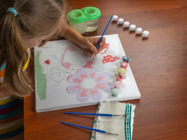 A little girls hand drawing with a brush and watercolor paints on white paper. Close-up. View from above. Creativity develops children.