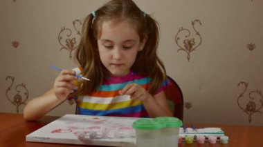 A girl of 7-8 years old sits at a table and draws a picture with paints on white paper. teaching children to draw.