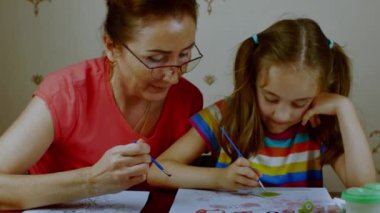 An adult woman with a little girl draws on paper with colored watercolors. Grandmother and granddaughter study painting. Preschool home education. High quality 4k footage.