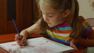 The girl sitting at the table enthusiastically draws with a brush and watercolor paints on a white canvas of paper. Drawing lessons for children and teenagers.