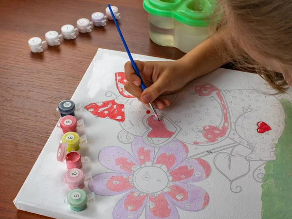 A little girls hand drawing with a brush and watercolor paints on white paper. Close-up. View from above. Creativity develops children.