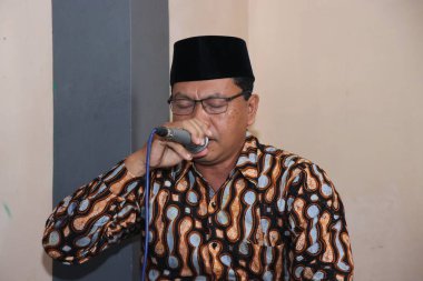 Batik 'te bir adam dua etmek için mikrofon tutuyor.