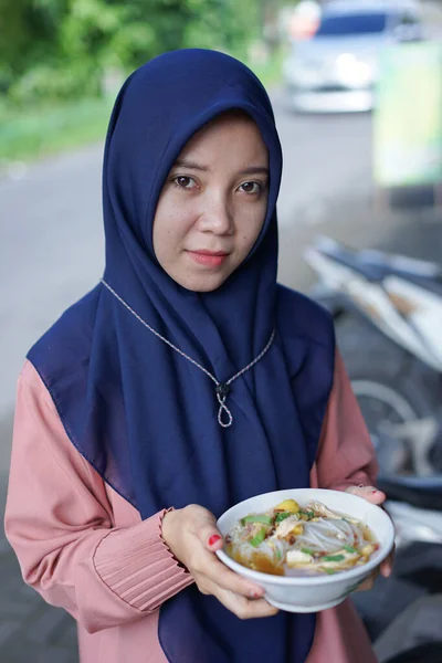 A veiled woman carrying a bowl of soup