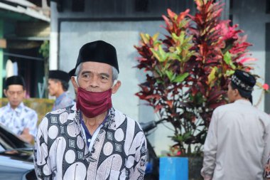 An old man with a maroon mask is glancing 