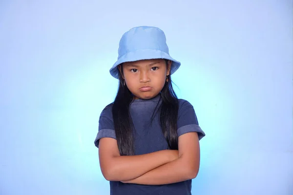 A child in a bad mood poses for the camera on a blue background