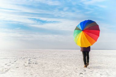 Gökkuşağı renkli şemsiyeli bir kadın donmuş denizde yürüyor. Parlak renkli kış manzarası 