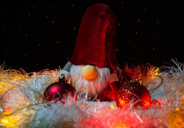 Oyuncak Yeni Yıl cücesi kırmızı Noel ağacı süslemeleri, beyaz süslemeler ve parlak çelenkler ile çevrili yıldızlı gökyüzünün taklidinin arka planında