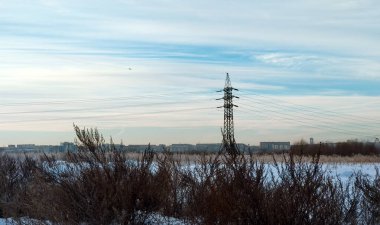 Elektrik hattı karlı bir alanda şehrin panoramasının ve gökyüzündeki uçağın arka planında duruyor.