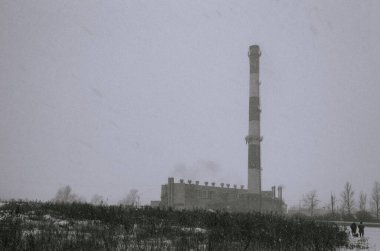 Ağır bir kar fırtınası sırasında, büyük bir kazan dairesinin önündeki küçük insanların siyah beyaz fotoğrafı.