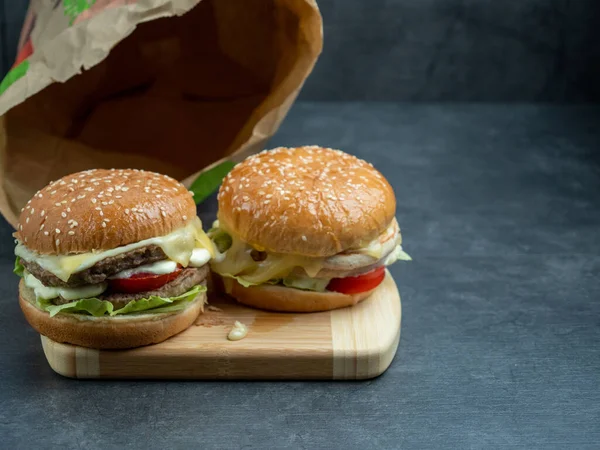 Hovězí burger se salátem, sýr na řezací desce na černém dřevěném stole. — Stock fotografie