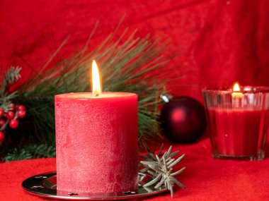 Kırmızı Noel mumu ve kırmızı arka planda Noel süslemeleri.