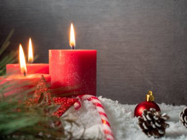Kırmızı Noel mumu ve gri arka planda Noel süslemeleri.