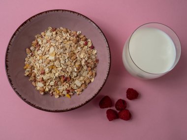 Muesli in a pink cup and a glass of milk on a pink table. Muesli on a pink background.