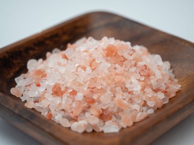 Beyaz arka planda pembe tuz bulunan ahşap bir kase..