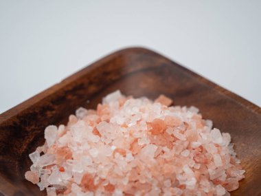 Beyaz arka planda pembe tuz bulunan ahşap bir kase..