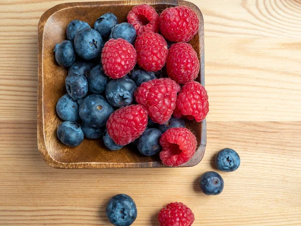 Ahşap bir arka planda ahududu ve yaban mersini. Taze ahududu ve yabanmersini..
