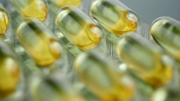 Brillante amarillo brillante píldoras Omega-3 envuelven sobre un fondo gris. — Vídeos de Stock