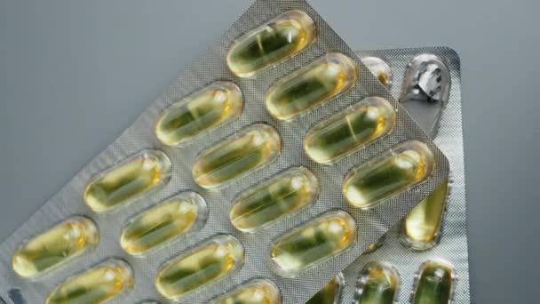 Pílulas brilhantes amarelas brilhantes Omega-3 enrolar em torno de um fundo cinza. — Vídeo de Stock