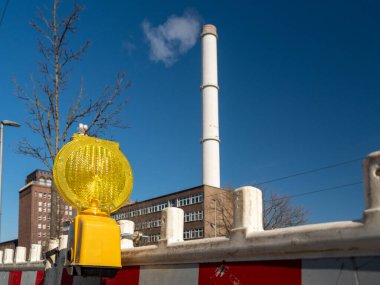 Dumanı tüten bir bacanın arka planında inşaat uyarı feneri