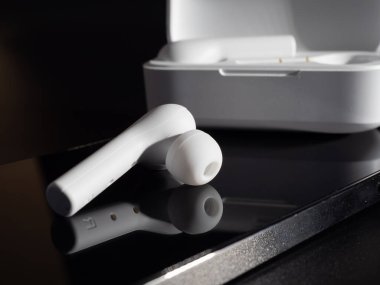 Siyah arka planda beyaz kablosuz kulaklık ve telefon.