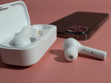 Pembe arka planda beyaz kablosuz kulaklık ve telefon.