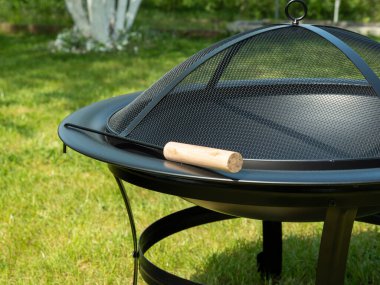 Metal bowl for fire on a background of green grass. Metal fire bowl with lid.