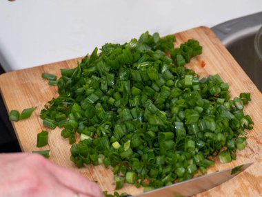 Kesme tahtasında yeşil soğan doğrayan bir elin parçası.