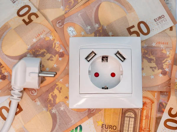 An electrical socket with a connected plug and euro banknotes around it. Electricity cost and expensive energy concept